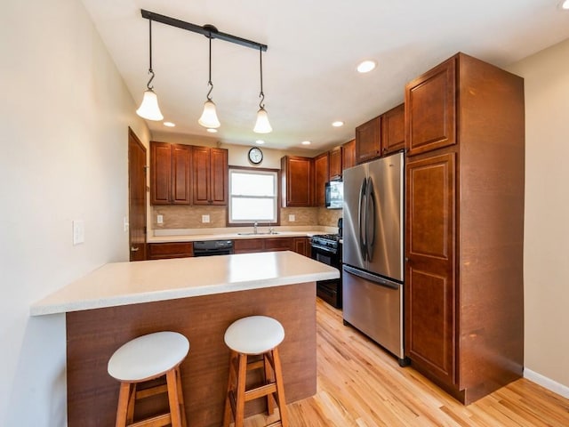 4634 Twin Pine Dr NE, Cedar Rapids, IA 52402 - kitchen featuring black appliances, a peninsula, a breakfast bar, light wood-style floors, and decorative backsplash
