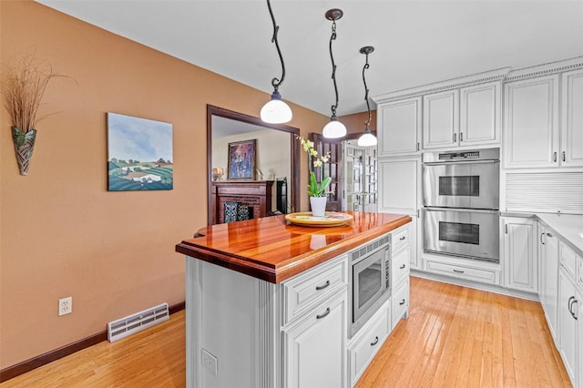 927 Southlawn Dr, Iowa City, IA 52245 - kitchen with appliances with stainless steel finishes, light wood-style flooring, white cabinetry, decorative light fixtures, and a center island