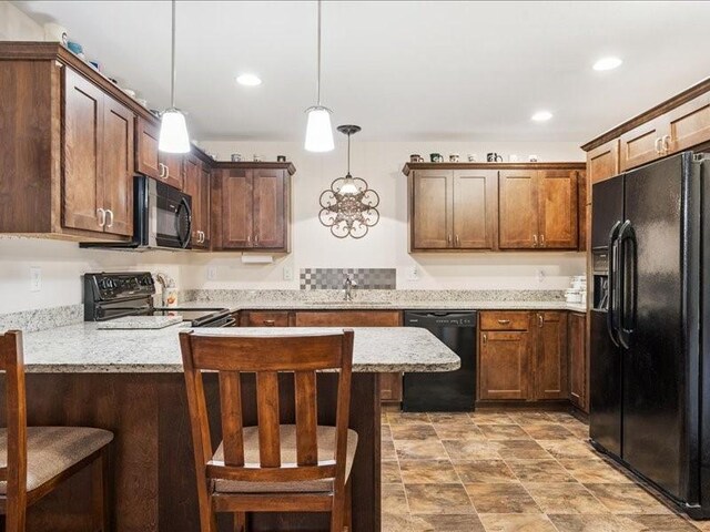 550 Meadow Oak Cir, Fairfax, IA 52228 - kitchen with black appliances, a breakfast bar area, hanging light fixtures, recessed lighting, and stone finish floors