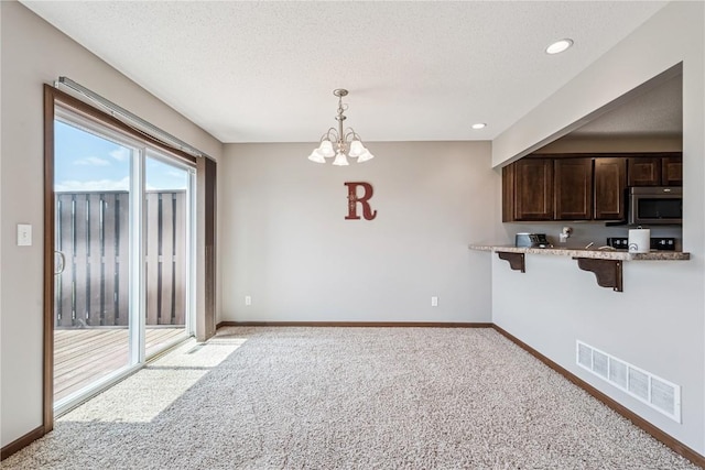 1019 Acacia Dr NE, Cedar Rapids, IA 52402 - kitchen with stainless steel microwave, a kitchen breakfast bar, light colored carpet, dark brown cabinets, and a chandelier