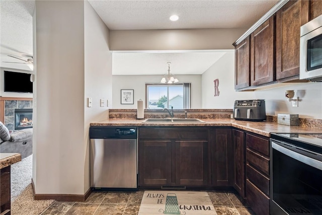 1019 Acacia Dr NE, Cedar Rapids, IA 52402 - kitchen with stainless steel appliances, dark brown cabinetry, a fireplace, a textured ceiling, and a ceiling fan