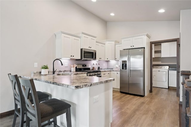 713 Hillside Dr, Tiffin, IA 52340 - kitchen with stainless steel appliances, washer / clothes dryer, a peninsula, white cabinets, and a kitchen bar
