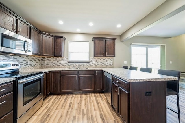 3212 Sherwood Pl, Marion, IA 52302 - kitchen featuring appliances with stainless steel finishes, a kitchen bar, light wood-type flooring, a peninsula, and dark brown cabinets