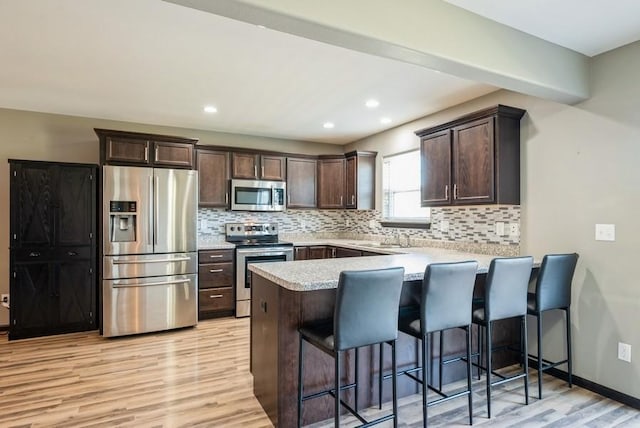 3212 Sherwood Pl, Marion, IA 52302 - kitchen featuring appliances with stainless steel finishes, light wood-style floors, a peninsula, dark brown cabinetry, and backsplash