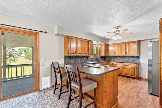 101 Golf Cir, Winfield, IA 52659 - kitchen with a peninsula, dark countertops, black electric stovetop, brown cabinetry, and a textured ceiling