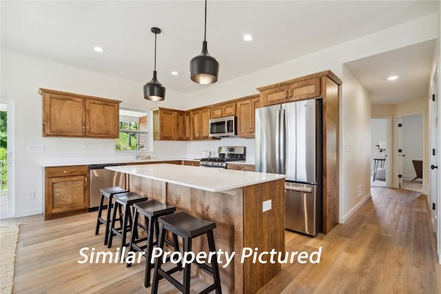 4620 Preston Ln, Iowa City, IA 52246 - kitchen with stainless steel appliances, brown cabinets, light wood-style floors, a kitchen island, and decorative light fixtures