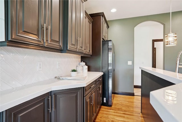5512 Black Oak Dr NE, Cedar Rapids, IA 52411 - kitchen featuring arched walkways, light countertops, decorative backsplash, light wood-type flooring, and dark brown cabinetry