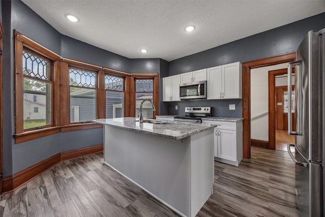 308 Main St, Norway, IA 52318 - kitchen with stainless steel appliances, white cabinets, an island with sink, light stone countertops, and a textured ceiling