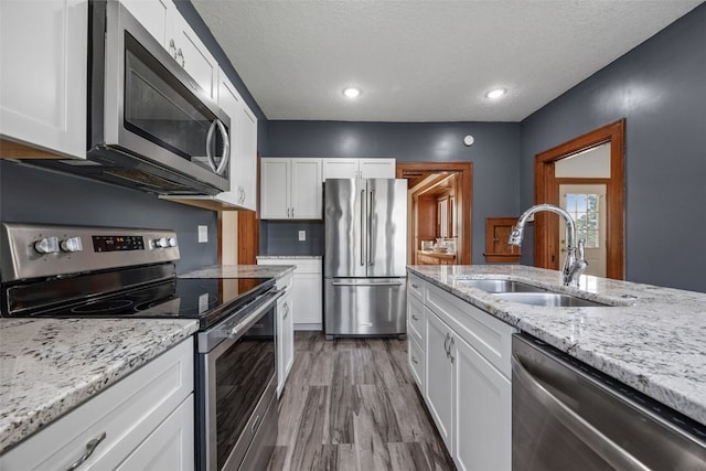 308 Main St, Norway, IA 52318 - kitchen featuring stainless steel appliances, white cabinets, a textured ceiling, wood finished floors, and light stone counters