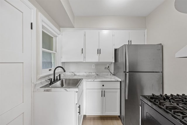2225 SE Mount Vernon Rd, Cedar Rapids, IA 52403 - kitchen featuring freestanding refrigerator, white cabinetry, black range with gas stovetop, light stone countertops, and light wood-style flooring