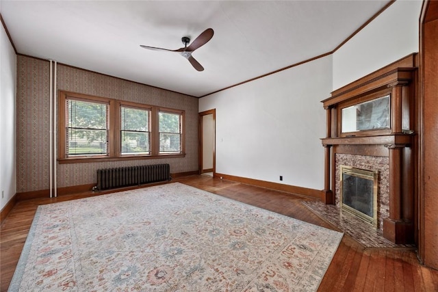 103 10th Ave SW, Mount Vernon, IA 52314 - unfurnished living room with radiator, wood finished floors, a stone fireplace, ceiling fan, and ornamental molding
