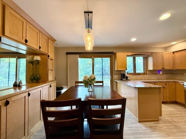 104 Oberlin St, Iowa City, IA 52245 - kitchen featuring light wood-style floors, decorative backsplash, a peninsula, light stone counters, and hanging light fixtures