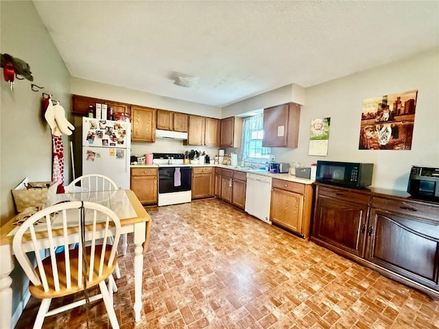 507 Maplewood Dr, Center Point, IA 52213 - kitchen with white appliances, under cabinet range hood, light countertops, brown cabinetry, and brick patterned floors