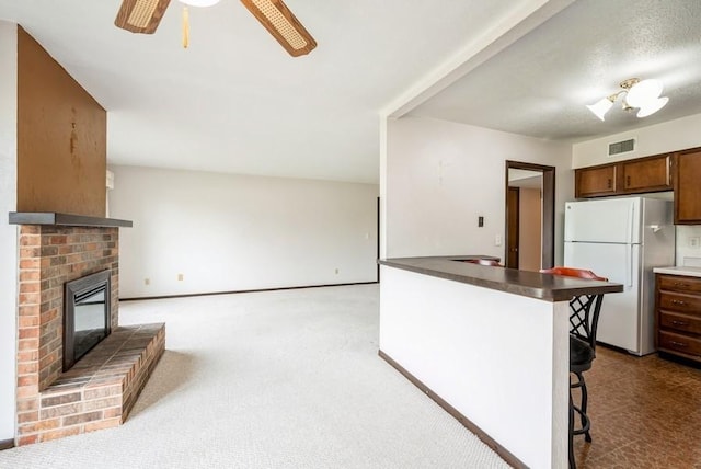 809 Kerry Ln SE Unit 66, Cedar Rapids, IA 52403 - kitchen featuring freestanding refrigerator, a brick fireplace, a breakfast bar area, a ceiling fan, and dark countertops