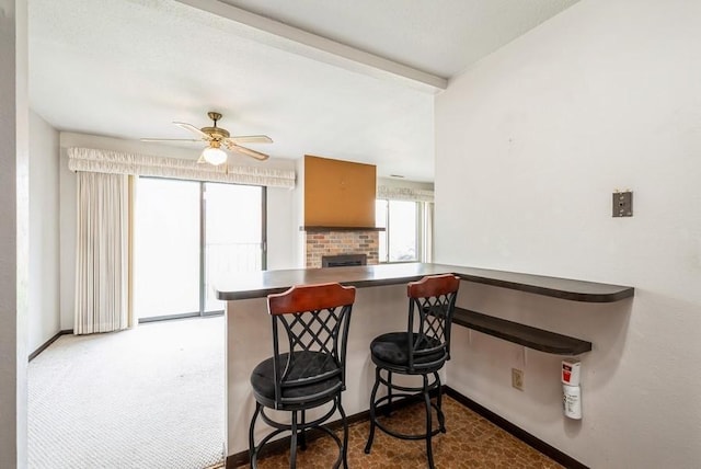 809 Kerry Ln SE Unit 66, Cedar Rapids, IA 52403 - kitchen featuring ceiling fan, a kitchen bar, dark countertops, and a brick fireplace
