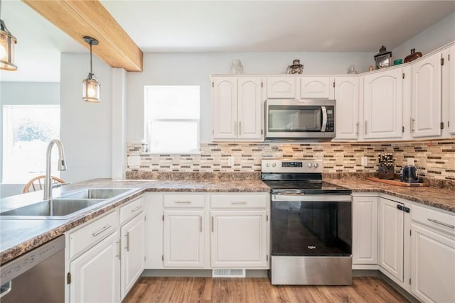 111 Maple St, Luzerne, IA 52257 - kitchen with stainless steel appliances, white cabinets, decorative backsplash, hanging light fixtures, and light wood-type flooring