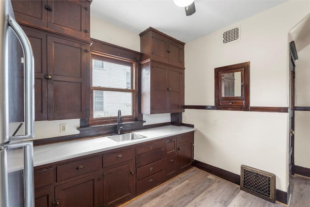 210 16th St SE, Cedar Rapids, IA 52403 - kitchen with stainless steel refrigerator, light wood-type flooring, ceiling fan, dark brown cabinetry, and light countertops
