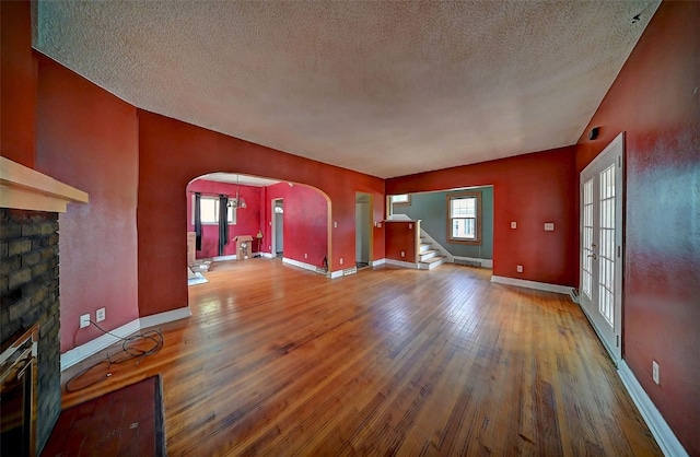 383 21st St SE, Cedar Rapids, IA 52403 - unfurnished living room featuring arched walkways, a fireplace, a textured ceiling, wood finished floors, and stairs