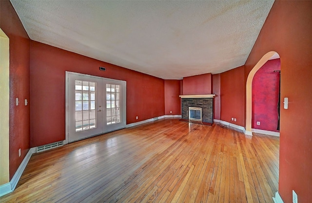 383 21st St SE, Cedar Rapids, IA 52403 - unfurnished living room featuring light wood-type flooring, arched walkways, a stone fireplace, a textured ceiling, and french doors
