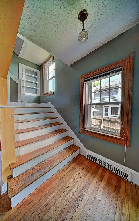 383 21st St SE, Cedar Rapids, IA 52403 - staircase featuring wood-type flooring, baseboard heating, and a textured ceiling