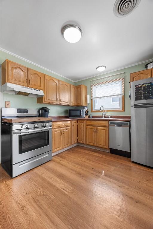 1140 31st St, Cedar Rapids, IA 52402 - kitchen with appliances with stainless steel finishes, under cabinet range hood, light wood-style flooring, and ornamental molding