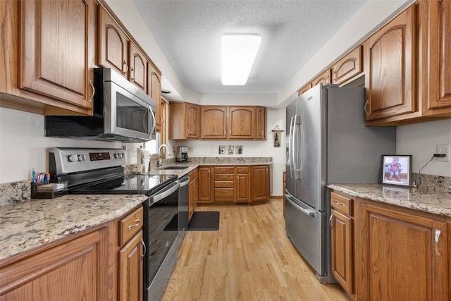 906 29th St NW, Cedar Rapids, IA 52405 - kitchen featuring stainless steel appliances, brown cabinets, light wood finished floors, light stone countertops, and a textured ceiling