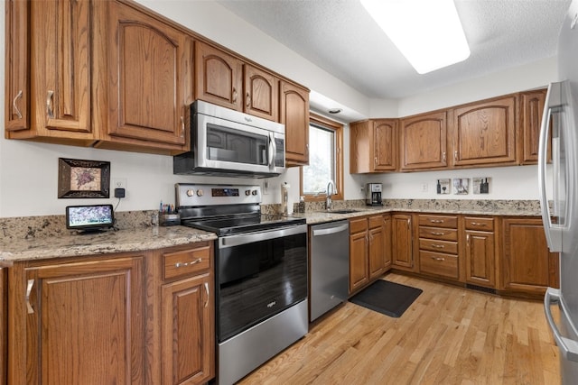 906 29th St NW, Cedar Rapids, IA 52405 - kitchen featuring appliances with stainless steel finishes, brown cabinets, light wood-style flooring, and light stone countertops