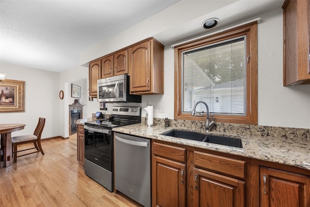 906 29th St NW, Cedar Rapids, IA 52405 - kitchen featuring appliances with stainless steel finishes, light wood finished floors, light stone counters, and brown cabinets