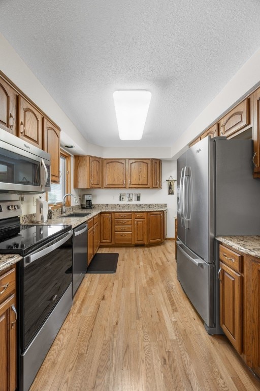 906 29th St NW, Cedar Rapids, IA 52405 - kitchen with appliances with stainless steel finishes, a textured ceiling, brown cabinets, and light wood-style flooring