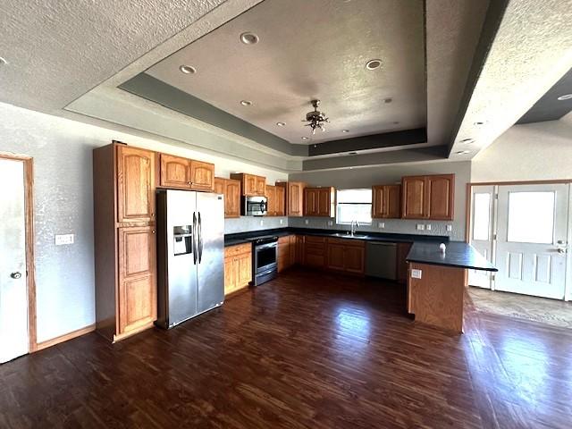 832 E Main St, Central City, IA 52214 - kitchen featuring stainless steel appliances, a tray ceiling, dark countertops, dark wood finished floors, and brown cabinetry