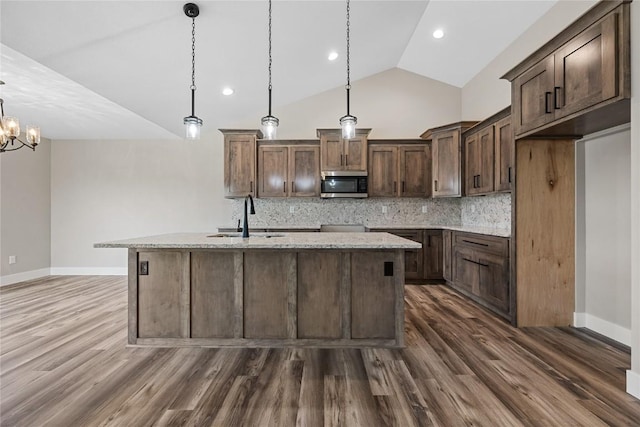 468 Chamber Dr, Anamosa, IA 52205 - kitchen featuring stainless steel microwave, tasteful backsplash, a kitchen island with sink, dark wood finished floors, and lofted ceiling