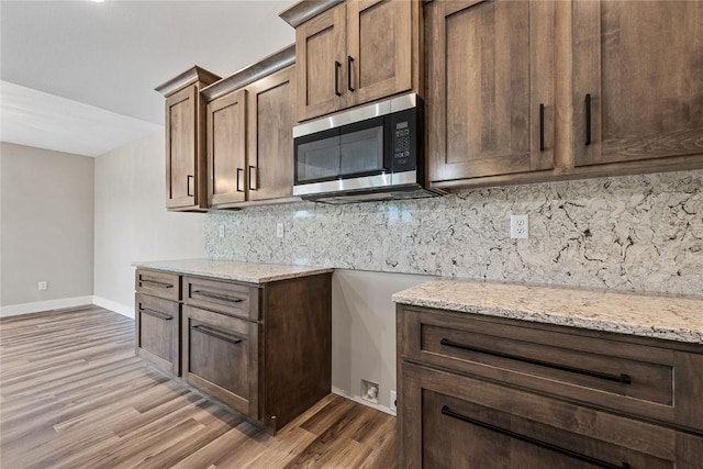 468 Chamber Dr, Anamosa, IA 52205 - kitchen with stainless steel microwave, light stone counters, light wood finished floors, and decorative backsplash
