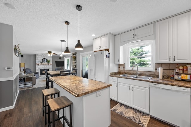 364 Essex Dr NE, Cedar Rapids, IA 52402 - kitchen with white appliances, a ceiling fan, a center island, a brick fireplace, and dark wood-style floors