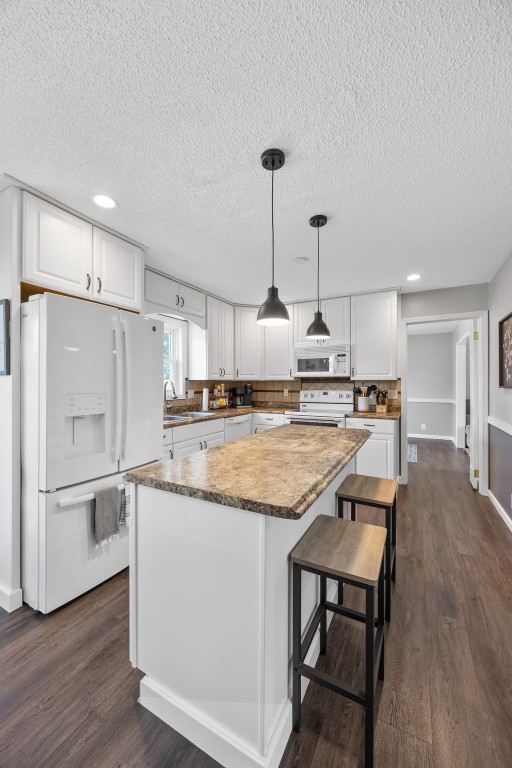 364 Essex Dr NE, Cedar Rapids, IA 52402 - kitchen with white appliances, a textured ceiling, white cabinetry, a center island, and dark wood-style floors