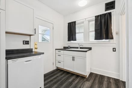 3107 E Ave NE, Cedar Rapids, IA 52402 - kitchen with white dishwasher, dark countertops, dark wood-style flooring, and white cabinetry