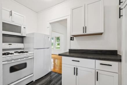 3107 E Ave NE, Cedar Rapids, IA 52402 - kitchen featuring white appliances, dark wood finished floors, dark countertops, white cabinets, and ornamental molding