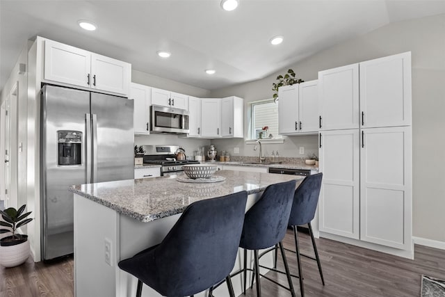 904 Hughes St, Coralville, IA 52241 - kitchen featuring appliances with stainless steel finishes, white cabinets, dark wood finished floors, a kitchen bar, and light stone counters