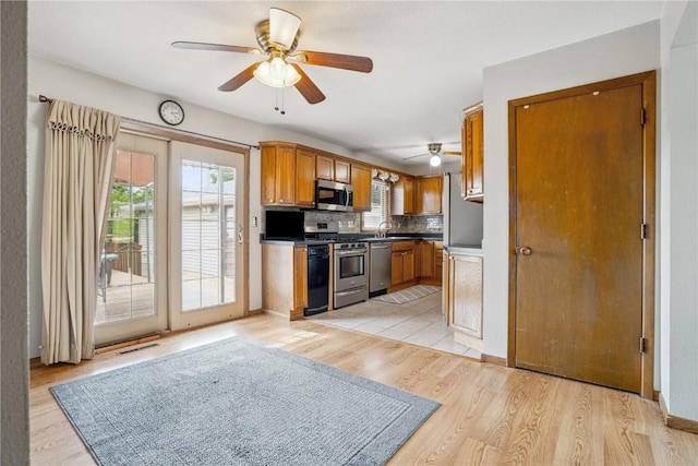 918 29th St NW, Cedar Rapids, IA 52405 - kitchen with appliances with stainless steel finishes, a ceiling fan, brown cabinetry, backsplash, and light wood-style flooring