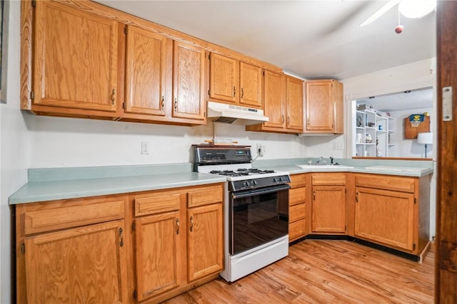 918 29th St NW, Cedar Rapids, IA 52405 - kitchen featuring white range with gas stovetop, under cabinet range hood, light countertops, light wood-style floors, and a ceiling fan