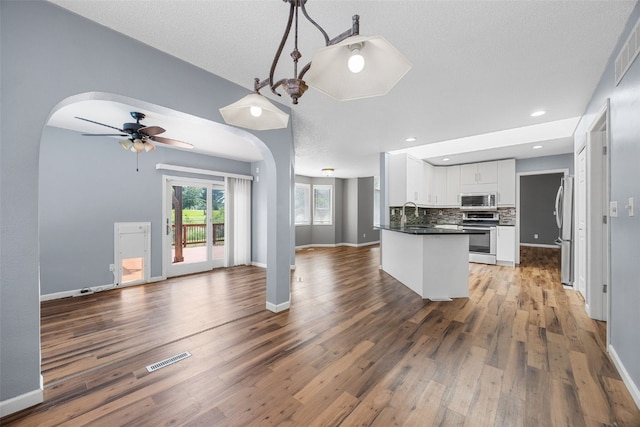 1125 Saint Andrews Dr, North Liberty, IA 52317 - kitchen with stainless steel appliances, open floor plan, dark countertops, white cabinetry, and wood finished floors