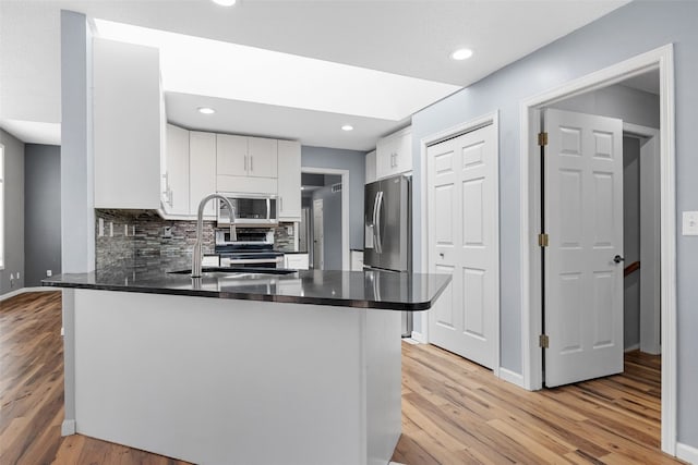 1125 Saint Andrews Dr, North Liberty, IA 52317 - kitchen with appliances with stainless steel finishes, light wood-type flooring, a peninsula, white cabinets, and backsplash