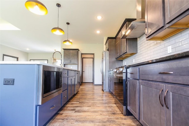 1600 Heartland St, Fairfax, IA 52228 - kitchen featuring wall chimney exhaust hood, appliances with stainless steel finishes, light wood finished floors, decorative backsplash, and pendant lighting