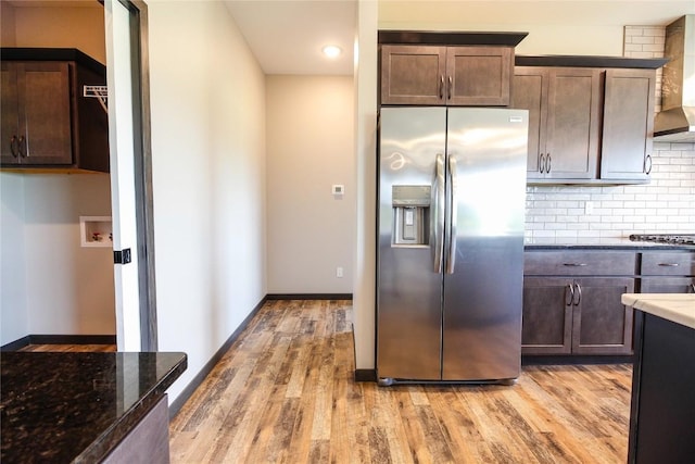 1600 Heartland St, Fairfax, IA 52228 - kitchen with stainless steel fridge, light wood-type flooring, dark stone countertops, wall chimney exhaust hood, and backsplash