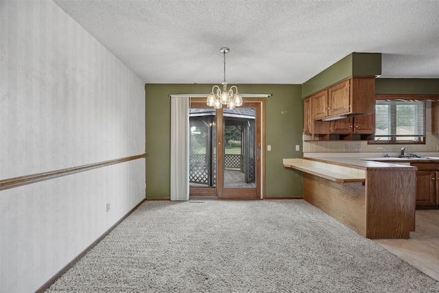 805 W 17th St, Vinton, IA 52349 - kitchen featuring a chandelier, a peninsula, hanging light fixtures, brown cabinets, and a textured ceiling