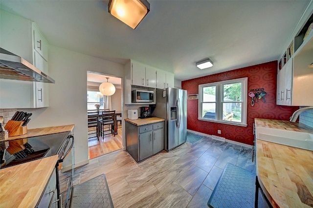 1175 28th St, Marion, IA 52302 - kitchen featuring wooden counters, stainless steel appliances, wallpapered walls, wall chimney exhaust hood, and white cabinets