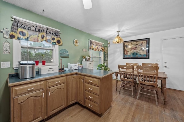 6613 Devonshire Dr NE, Cedar Rapids, IA 52402 - kitchen featuring light wood finished floors, a peninsula, dark countertops, brown cabinets, and decorative light fixtures
