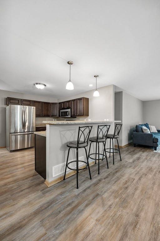 1458 Tower Ln NE Unit 12, Cedar Rapids, IA 52402 - kitchen with stainless steel appliances, dark brown cabinetry, a kitchen breakfast bar, light wood-style floors, and decorative light fixtures