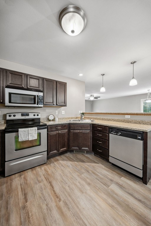 1458 Tower Ln NE Unit 12, Cedar Rapids, IA 52402 - kitchen with appliances with stainless steel finishes, dark brown cabinets, light wood-type flooring, decorative light fixtures, and a peninsula