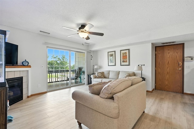 3060 Wilson Ave SW Unit 7, Cedar Rapids, IA 52404 - living room with light wood-style flooring, a textured ceiling, a ceiling fan, and a tiled fireplace