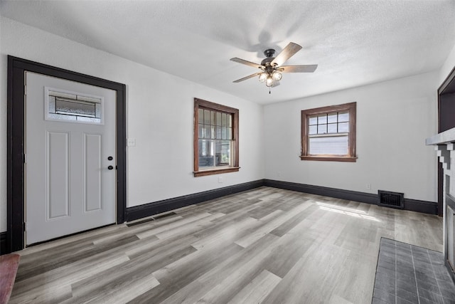 1818 Park Ave SE, Cedar Rapids, IA 52403 - unfurnished living room featuring light wood-style flooring, a ceiling fan, a fireplace with flush hearth, and a textured ceiling